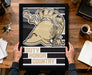 A person is holding up a framed poster with a graphic design featuring a helmet and the text "DUTY HONOR COUNTRY".