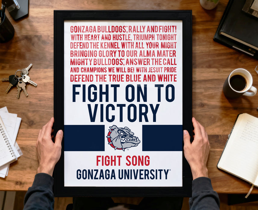 a person holding a framed poster with text and a bulldog logo, placed on a wooden desk.