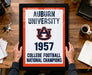 A framed sign displaying the text "Auburn University 1957 College Football National Champions" is being held by a person's hands.