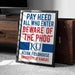A framed sign with the text "PAY HEED ALL WHO ENTER BEWARE OF THE PHOG" and "ALLEN FIELDHOUSE UNIVERSITY OF KANSAS" on it, placed on a carpeted floor next to a wooden dresser.
