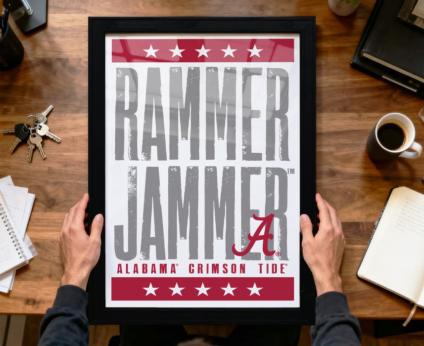 A framed poster with the text "RAMMER JAMMER" and "ALABAMA CRIMSON TIDE" is being held by a person's hands.