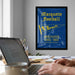 a framed poster of Marquette Football with a person working on a laptop at a desk in the foreground.