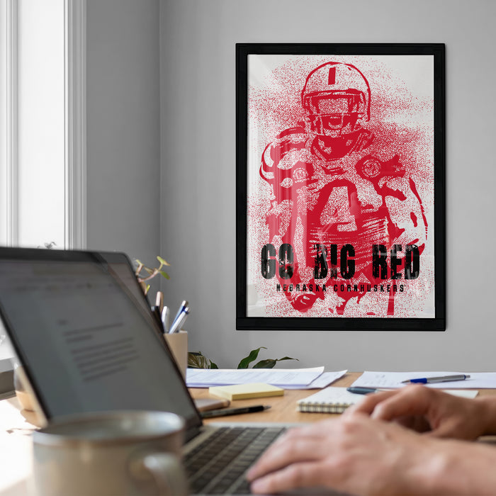 a framed poster of a football player on the wall, with a laptop and a coffee cup on a desk in the foreground.