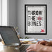 a framed poster with the text "THROW THE BONES" and a football helmet graphic, hanging on a wall above a desk with a laptop and other office supplies.