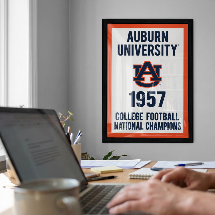 a framed poster of Auburn University from 1957, with a person's hands typing on a laptop in the foreground.