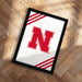 A framed poster with the letter "N" on it, placed on a wooden floor.