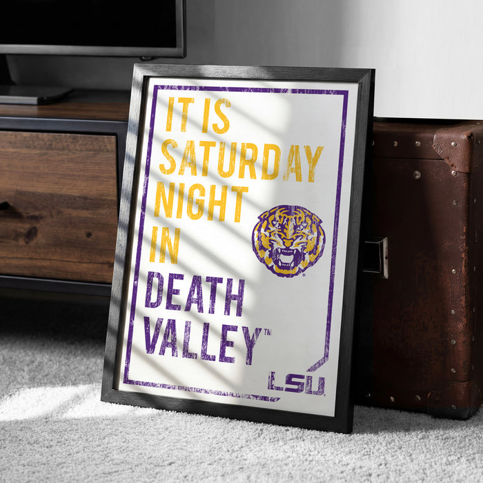 A framed poster with text and a tiger logo, placed on a carpeted floor next to a wooden chest.