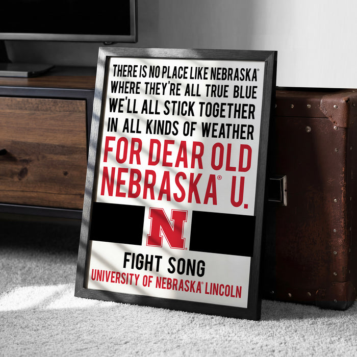 a framed poster with text that reads "There is no place like Nebraska where they're all true blue we'll all stick together in all kinds of weather for dear old Nebraska U. FIGHT SONG UNIVERSITY OF NEBRASKA LINCOLN".