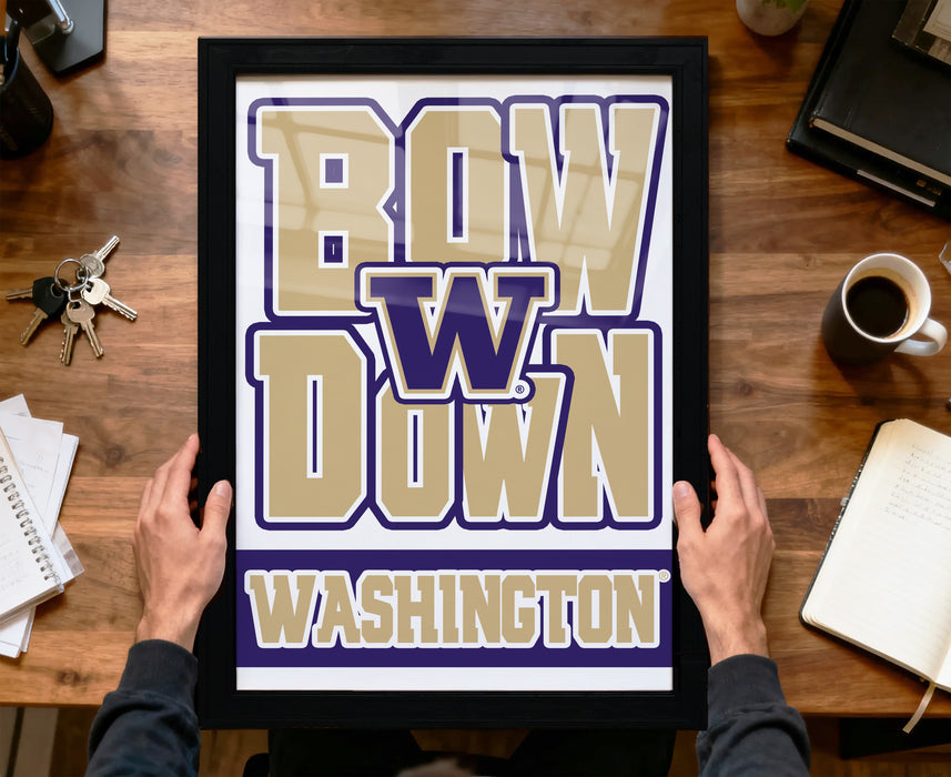 A framed poster with the text "BOW W down Washington" is being held by a person's hands, with a wooden desk and various items such as keys, a cup, and a notebook visible in the background.