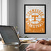 a person working on a laptop at a desk, with a framed poster of the Tennessee Basketball logo hanging on the wall behind them.