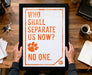 A person is holding up a framed poster with the text "WHO SHALL SEPARATE US NOW? NO ONE." The poster features a paw print and a key, suggesting a message related to separation or exclusivity.