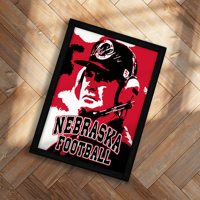 A framed poster featuring a close-up of a person wearing a Nebraska football helmet, with the text "NEBRASKA FOOTBALL" prominently displayed.