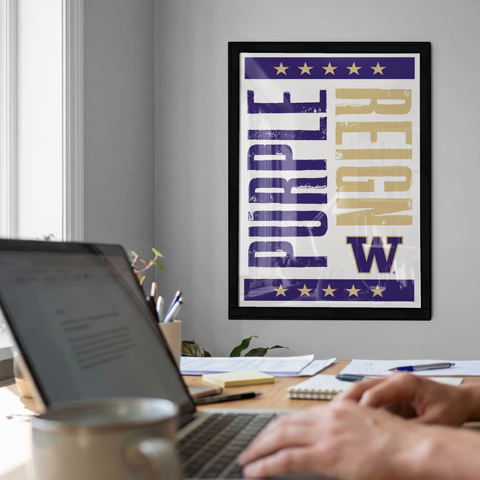 a person working on a laptop at a desk, with a framed poster featuring the word "Purple" and " Reign" on the wall behind them.