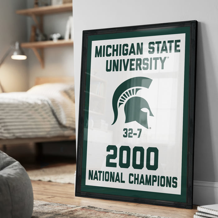 A framed poster celebrating the Michigan State University's 32-7 National Champions, with the text "MICHIGAN STATE UNIVERSITY 32-7 2000 NATIONAL CHAMPIONS" prominently displayed.