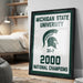 A framed poster celebrating the Michigan State University's 32-7 National Champions, with the text "MICHIGAN STATE UNIVERSITY 32-7 2000 NATIONAL CHAMPIONS" prominently displayed.
