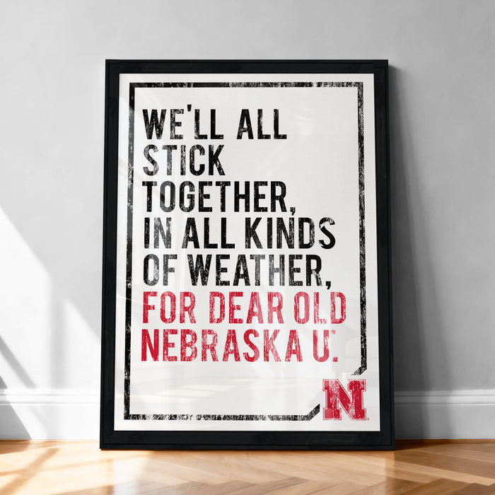 The image is a framed poster with the text "WE'LL ALL STICK TOGETHER, IN ALL KINDS OF WEATHER, FOR DEAR OLD NEBRASKA U."