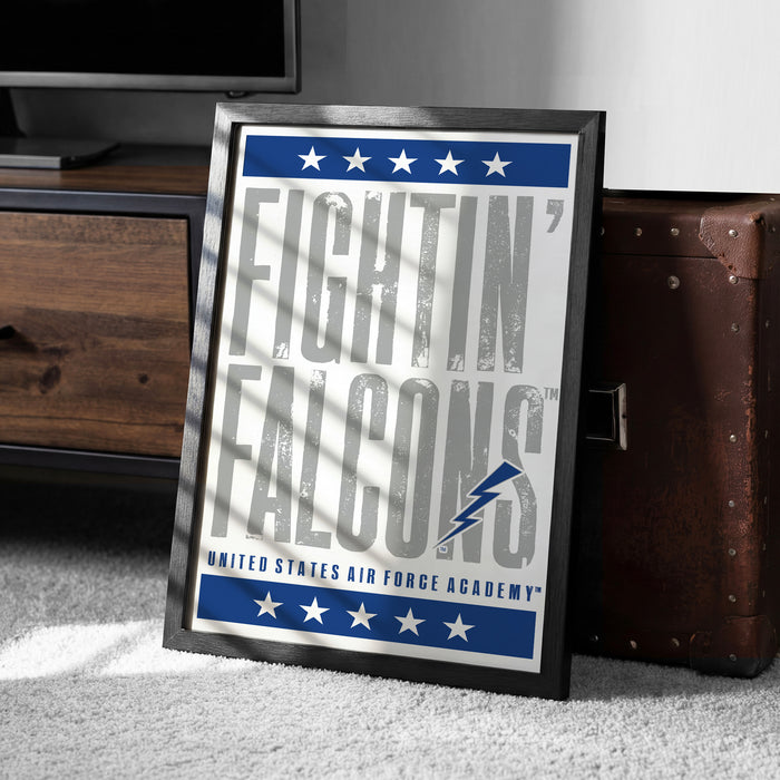 a framed poster with the text "FIGHTIN' FALCONS" and "UNITED STATES AIR FORCE ACADEMY" printed on it. The poster is placed on a carpeted floor next to a wooden cabinet.