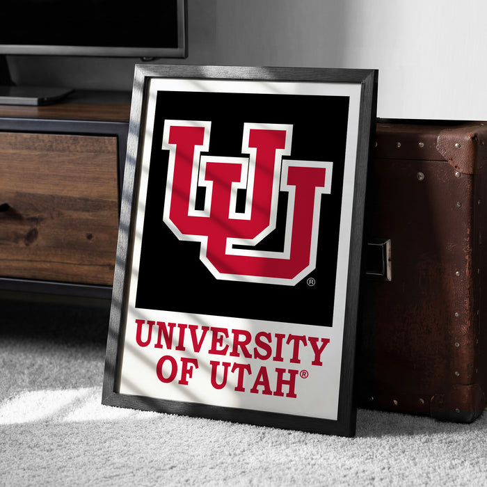 A framed poster of the University of Utah logo is displayed on a carpeted floor next to a wooden chest.