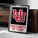 A framed poster of the University of Utah logo is displayed on a carpeted floor next to a wooden chest.