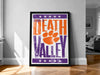 A framed poster with the text "Welcome to Death Valley" and an orange paw print, displayed on a wall in a room.