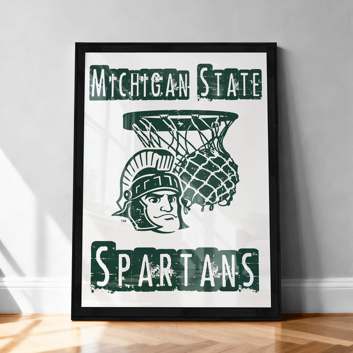 A framed poster featuring the Michigan State Spartans basketball team logo, with a basketball hoop and a person wearing a Spartans helmet.