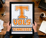 A person is holding a framed picture of the Tennessee State University (TSU) logo, which is an orange letter "T" with a registered trademark symbol.