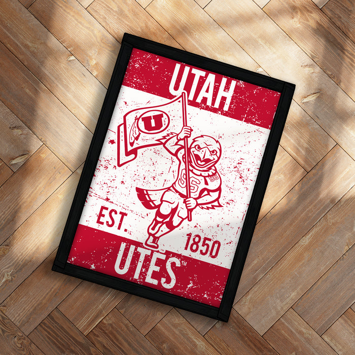 A framed poster with a red and white design featuring a bird holding a flag and the text "UTAH EST. 1850 UTES".