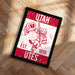 A framed poster with a red and white design featuring a bird holding a flag and the text "UTAH EST. 1850 UTES".