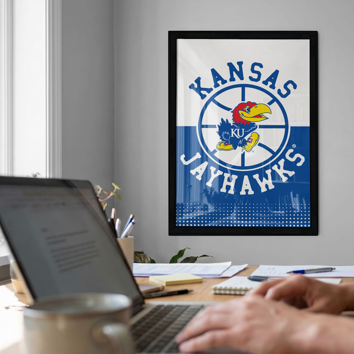 a framed poster of the Kansas Jayhawks basketball team on the wall, with a person's hands typing on a laptop in the foreground.
