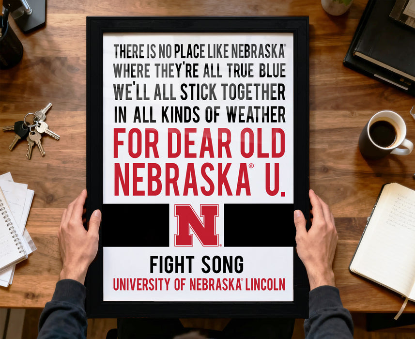 a framed poster with text that reads "There is no place like Nebraska where they're all true blue we'll all stick together in all kinds of weather for dear old Nebraska U. Fight Song University of Nebraska Lincoln".