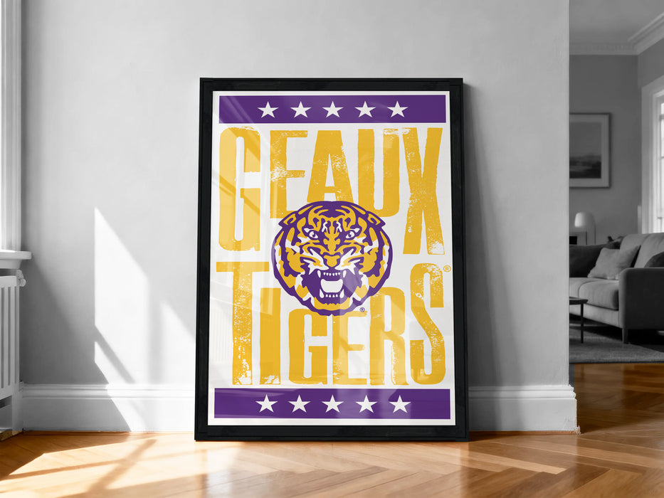 A framed poster with the text "GEAUX TIGERS" and a tiger graphic, placed on a wooden floor against a white wall.