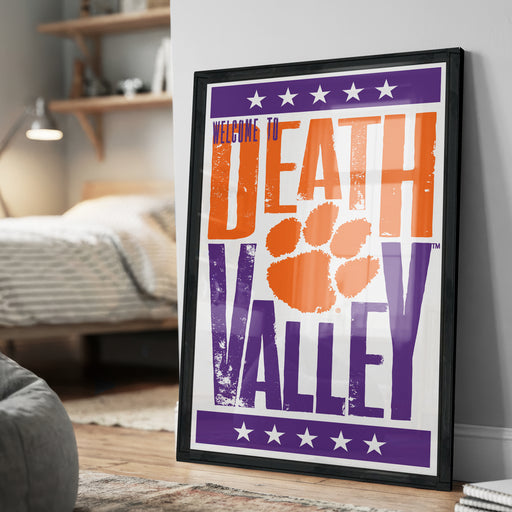 A framed poster with the text "Welcome to Death Valley" and an orange paw print, placed on a wall in a bedroom.