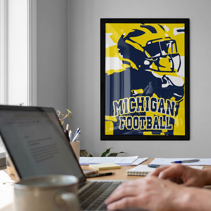 a framed poster of a football player on the wall, with a laptop and a coffee cup on a desk in front of it.