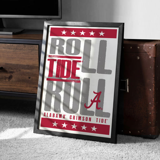 A framed poster with the text "ROLL TIDE RULL" and "ALABAMA'S GRIMSON TIDE" printed on it, placed on a carpeted floor next to a wooden chest.