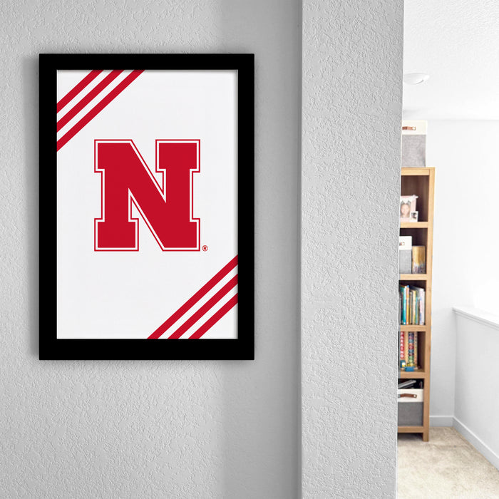 a framed poster with a large red letter "N" on a white background, hanging on a wall.