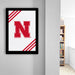 a framed poster with a large red letter "N" on a white background, hanging on a wall.