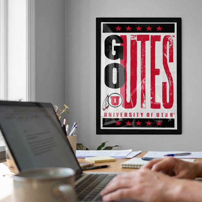A framed poster with the text "GO TES" is displayed on the wall above a desk with a laptop and other office supplies.