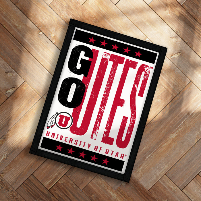 A framed poster with the text "GO OUTS" and "UNIVERSITY OF UTAH" printed on it, placed on a wooden floor.