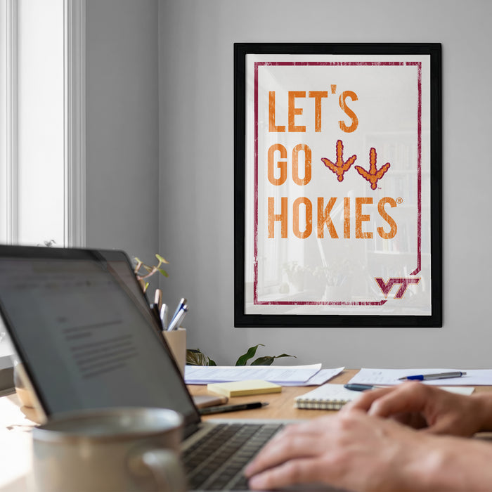 a person working on a laptop at a desk, with a framed poster on the wall behind them that says "LET'S GO HOKIES".