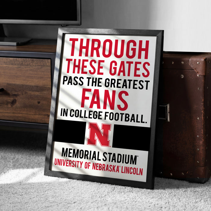 A framed sign with text that reads "THROUGH THESE GATES PASS THE GREATEST FANS IN COLLEGE FOOTBALL. MEMORIAL STADIUM UNIVERSITY OF NEBRASKA LINCOLN"