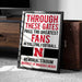 A framed sign with text that reads "THROUGH THESE GATES PASS THE GREATEST FANS IN COLLEGE FOOTBALL. MEMORIAL STADIUM UNIVERSITY OF NEBRASKA LINCOLN"