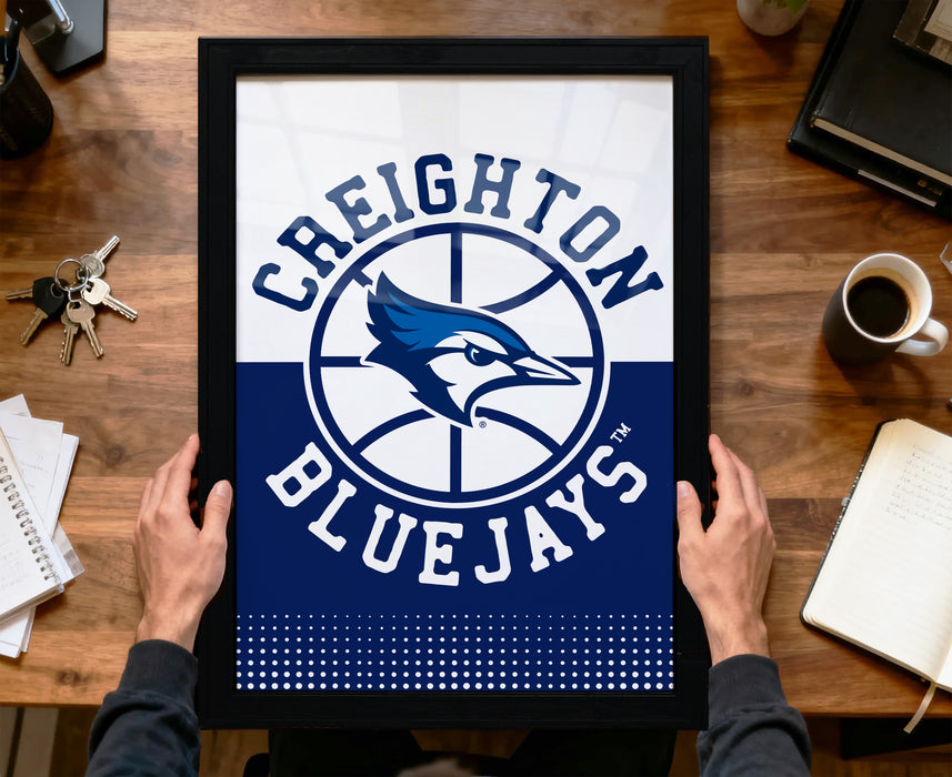 A framed poster of the Toronto Blue Jays basketball team logo is being held by a person's hands, with a desk and various items such as keys, a cup, and a notebook visible in the background.