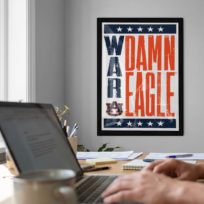 a framed poster with the text "DAMN EAGLE" on it, which is displayed on a wall above a desk with a laptop and other items.