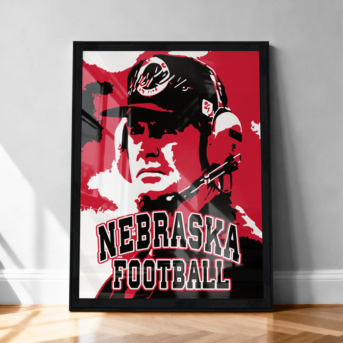 A framed poster featuring a close-up portrait of a person wearing a baseball cap and the text "NEBRASKA FOOTBALL" prominently displayed.