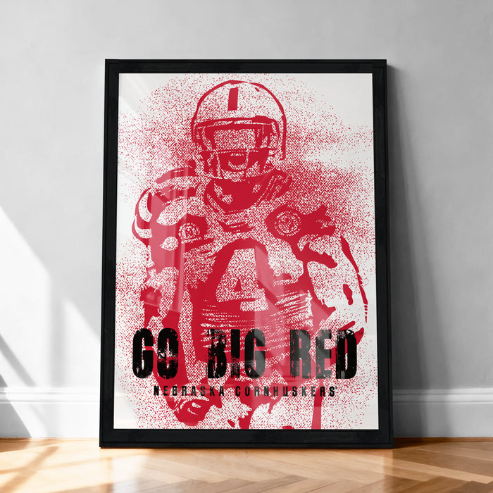 The image is a framed poster featuring a red and black design of a football player, with the text "Go Big Red Nebraska Cornhussers" prominently displayed.