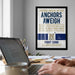 a framed poster with a humorous message about anchors and a naval school, hanging on a wall above a desk with a laptop and other items.