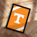 a framed poster with the letter "T" on it, placed on a wooden floor.