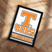 A framed poster with the word "TENNESSEE" printed on it, placed on a wooden floor.