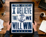 A framed poster with the text "I BELIEVE THAT WE WILL WIN" is being held by a person's hands, with a wooden desk and various items such as a cup, keys, and a notebook in the background.