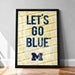 A framed poster with the text "LET'S GO BLUE! LET'S GO" printed on it, along with the letters "BLUE! LET'S" repeated multiple times in a yellow and black pattern.